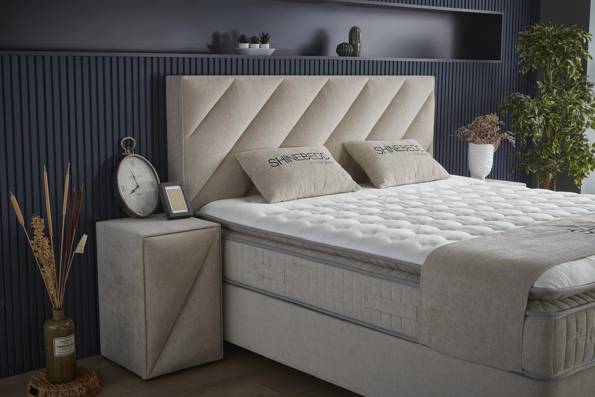 Nahaufnahme eines Boxspringbetts von SkyHome24.de mit dekorativem Kissen und Wanduhr mit römischen Ziffern, ideal für stilvolles und günstiges Innendesign.