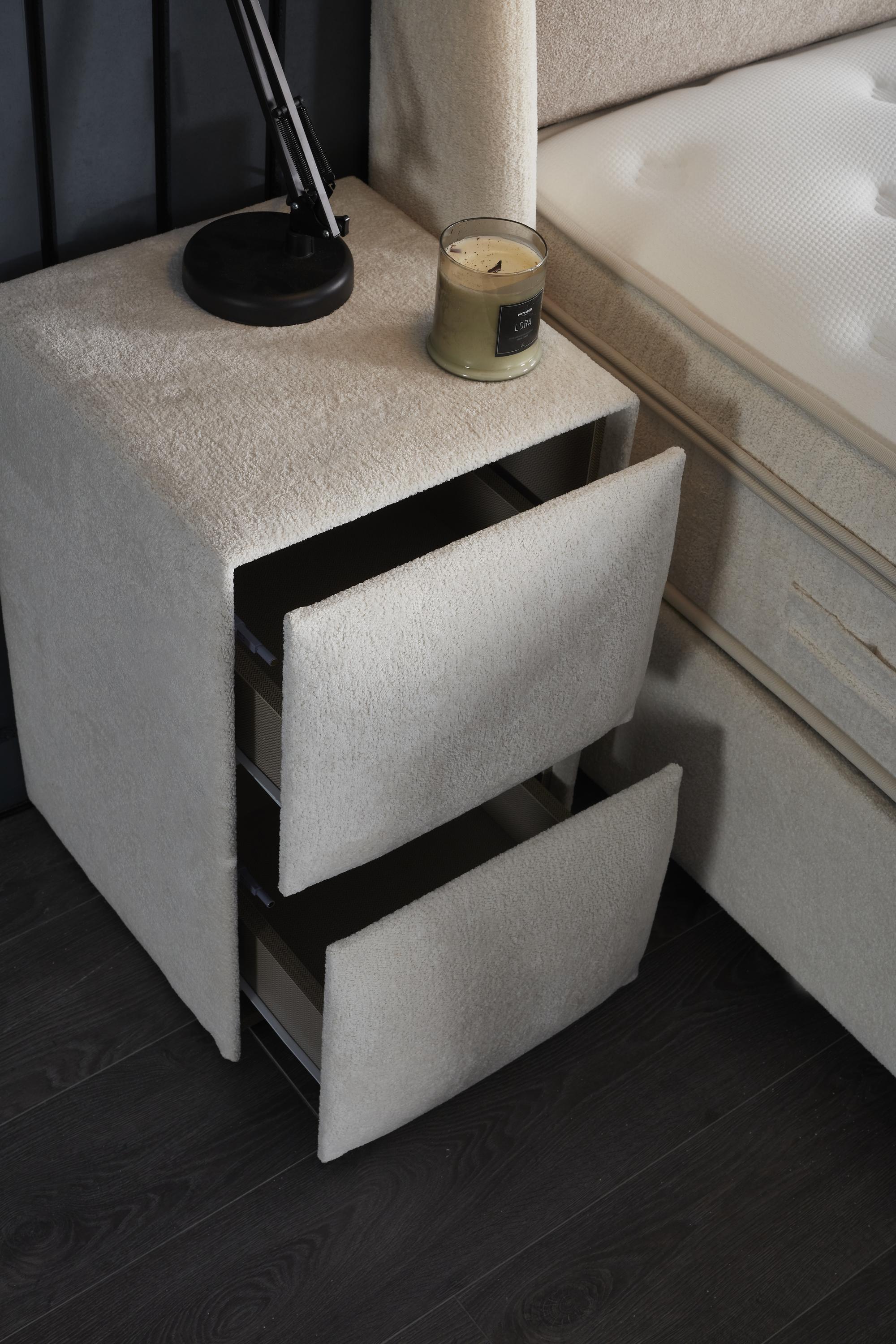 Boxspringbett 'TwinBedd' von SkyHome24.de, stilvoll mit Matratze und Stauraum, auf einem eleganten Nachtisch, betont durch eine Kerze und Lampe.