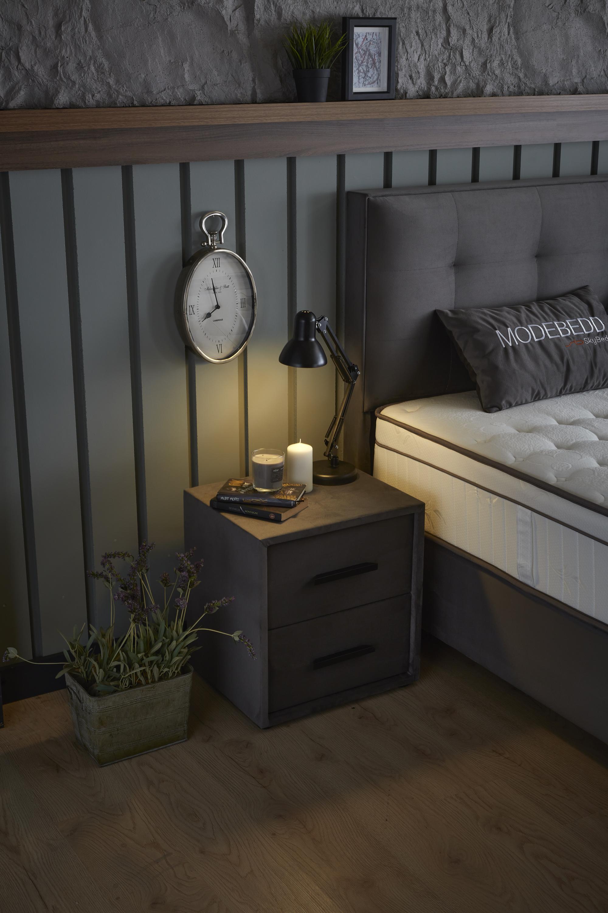 Boxspringbett 'ModeBedd' von SkyBedd mit Matratze und Stauraum, gezeigt auf einer Kommode mit Pflanze, Uhr und Kerze.