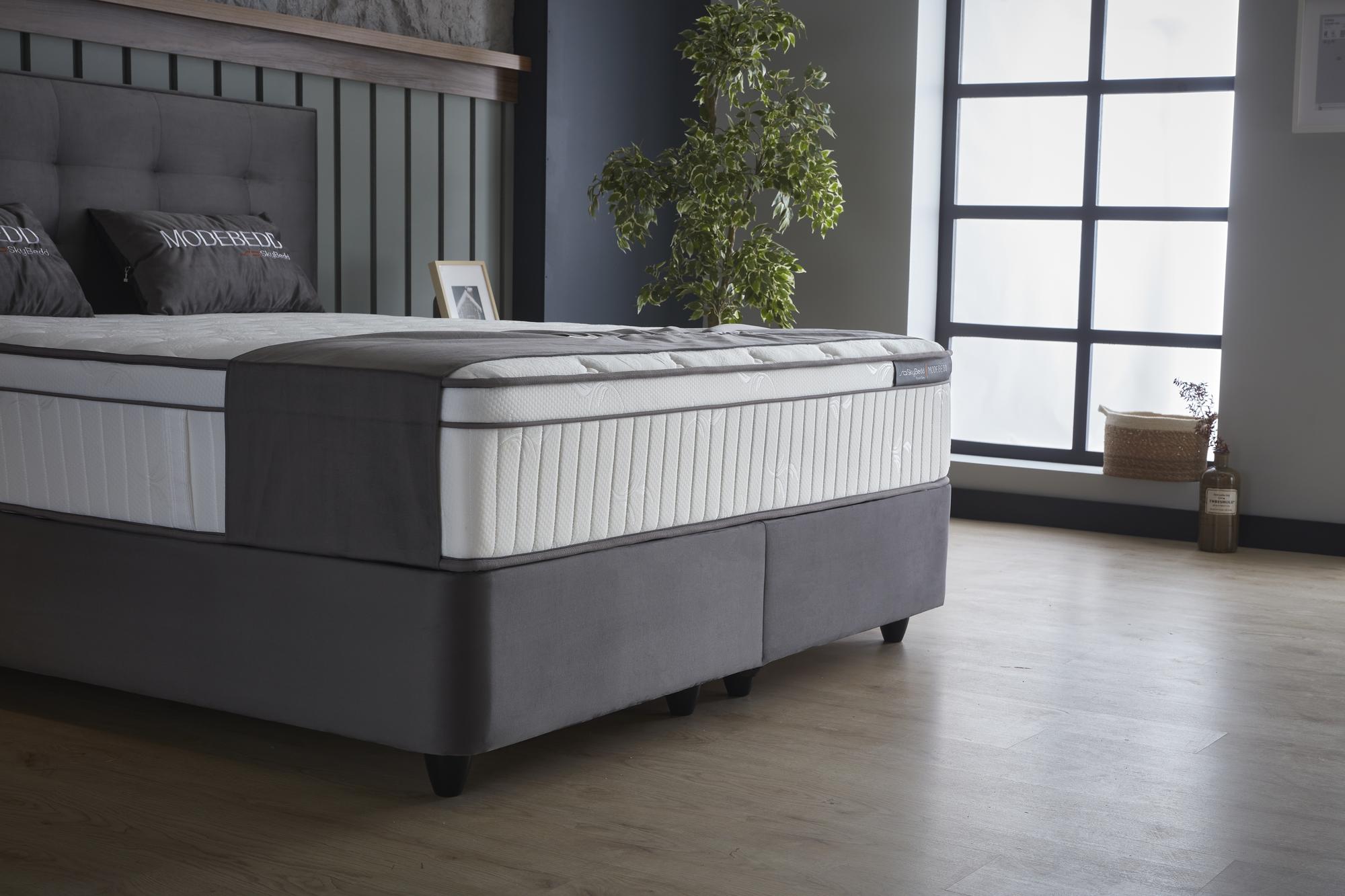 Boxspringbett 'ModeBedd' SkyBedd mit ergonomischer Matratze und integriertem Stauraum, kombiniert Coil Pro Balance Spring Technology mit Softschaum, im Schlafzimmer platziert.