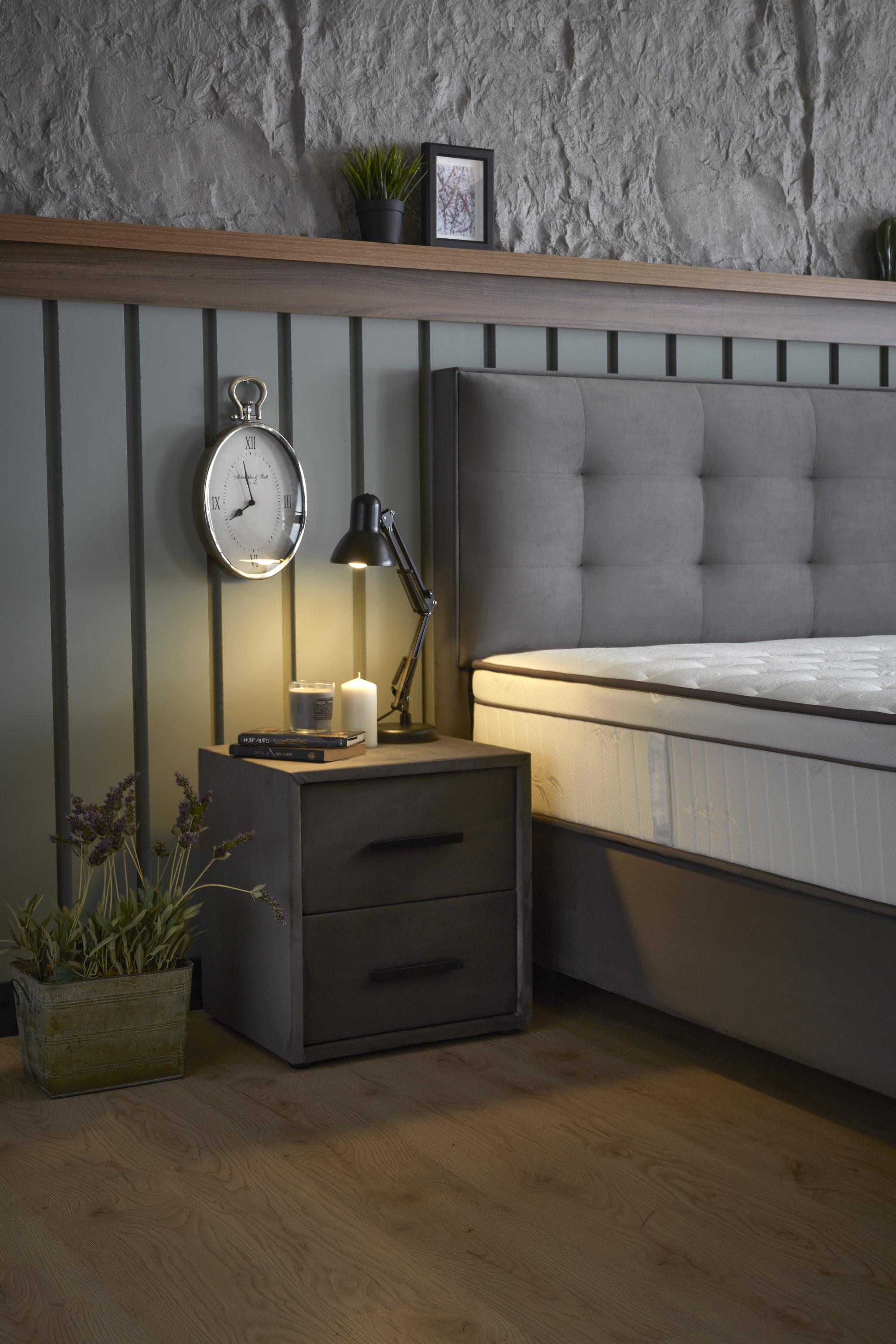 Boxspringbett 'ModeBedd' SkyBedd mit ergonomischer Hybridmatratze und integriertem Stauraum, präsentiert zwischen Uhr und Pflanze, ideal für stressfreies Entspannen.