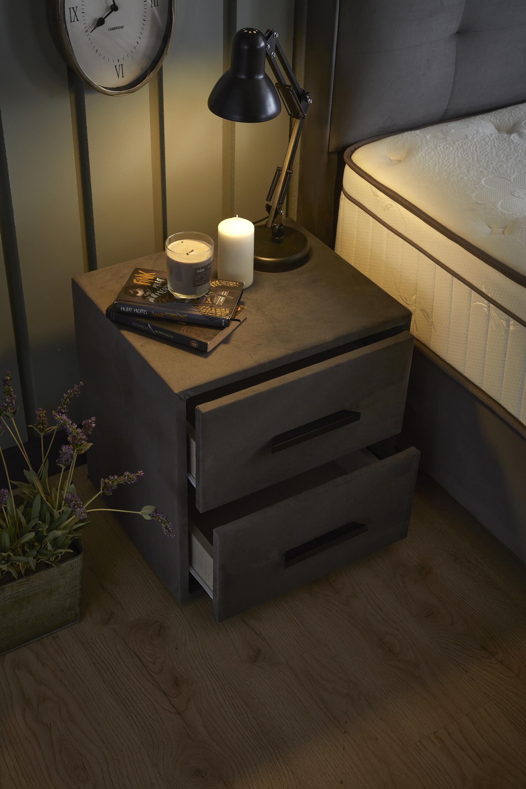 Boxspringbett 'ModeBedd' SkyBedd in Grau/Anthrazit mit ergonomischer Matratze und integriertem Stauraum, umgeben von Lampe, Pflanze und Kerze.