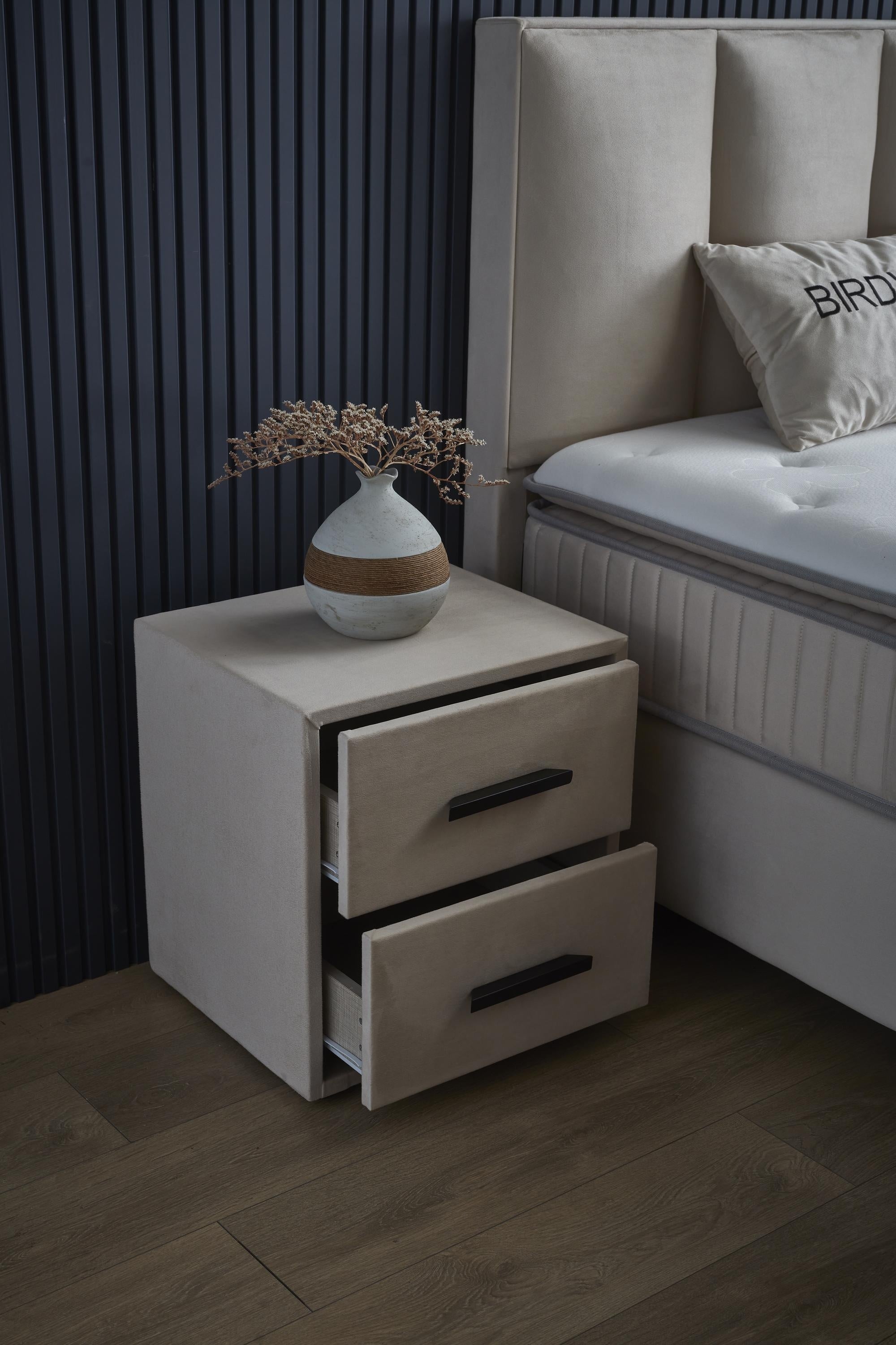 Boxspringbett 'BirdyBedd' SkyBedd in Beige mit integrierter Stauraum-Matratze, präsentiert in einem Schlafzimmer-Setting mit Nachttisch und Blumenvase.