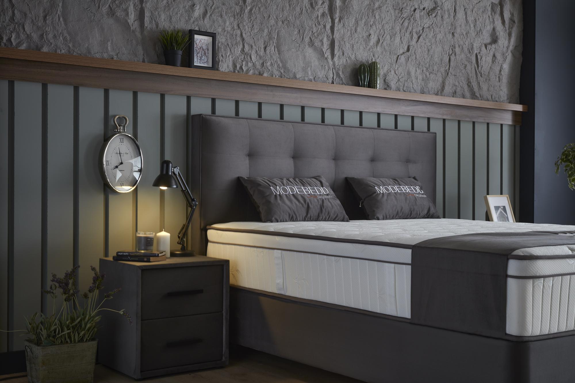 Boxspringbett 'ModeBedd' SkyBedd mit ergonomischer Matratze und integriertem Stauraum, präsentiert auf einem stilvollen, modernen Hintergrund mit dekorativen Accessoires.